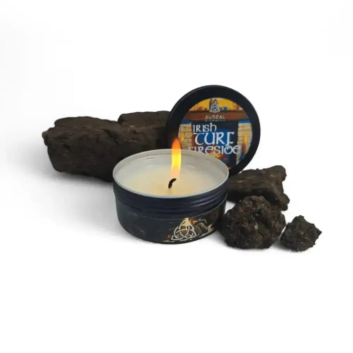 Lit Irish Turf Fireside candle in a black tin beside its lid and pieces of dried turf